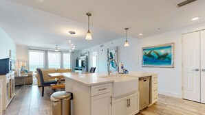 A modern kitchen with white cabinetry, a central island, and pendant lighting. - Blu 305 - Gulf-front condo with upgraded features - quick drive to entertainment (Fort Walton Beach)