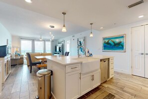 A modern kitchen with white cabinetry, a central island, and pendant lighting. - Blu 305 - Gulf-front condo with upgraded features - quick drive to entertainment (Fort Walton Beach)