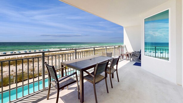 A balcony with a view of the ocean, a pool, and a dining area with chairs and a table. - Blu 305 - Gulf-front condo with upgraded features - quick drive to entertainment (Fort Walton Beach)