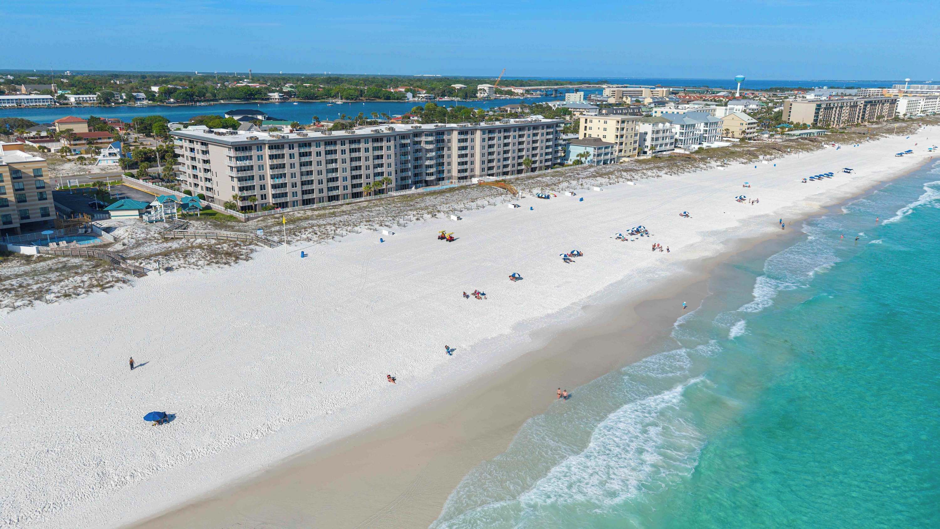 Une plage avec un hôtel en arrière-plan, un ciel dégagé et une mer calme.