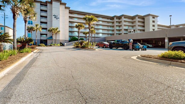 A hotel with multiple floors, palm trees, and a parking area with several vehicles. - Second-floor, airy condo with great views - close to dining & shopping (Fort Walton Beach)