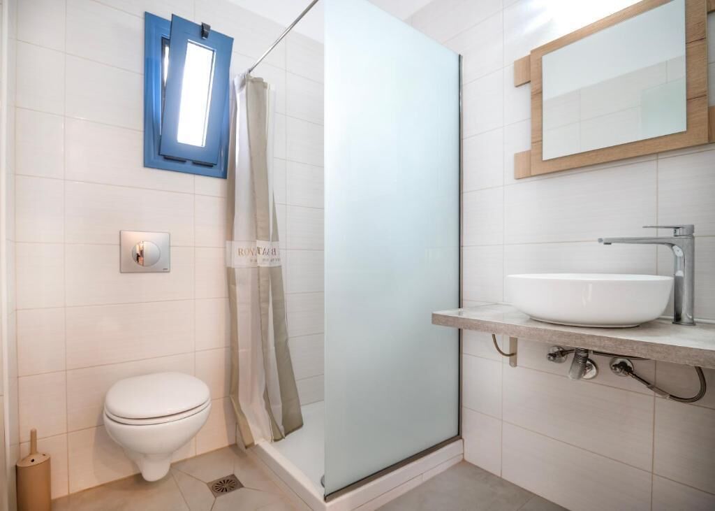 A modern bathroom with a glass shower enclosure, a white toilet, and a sink with a mirror above it.