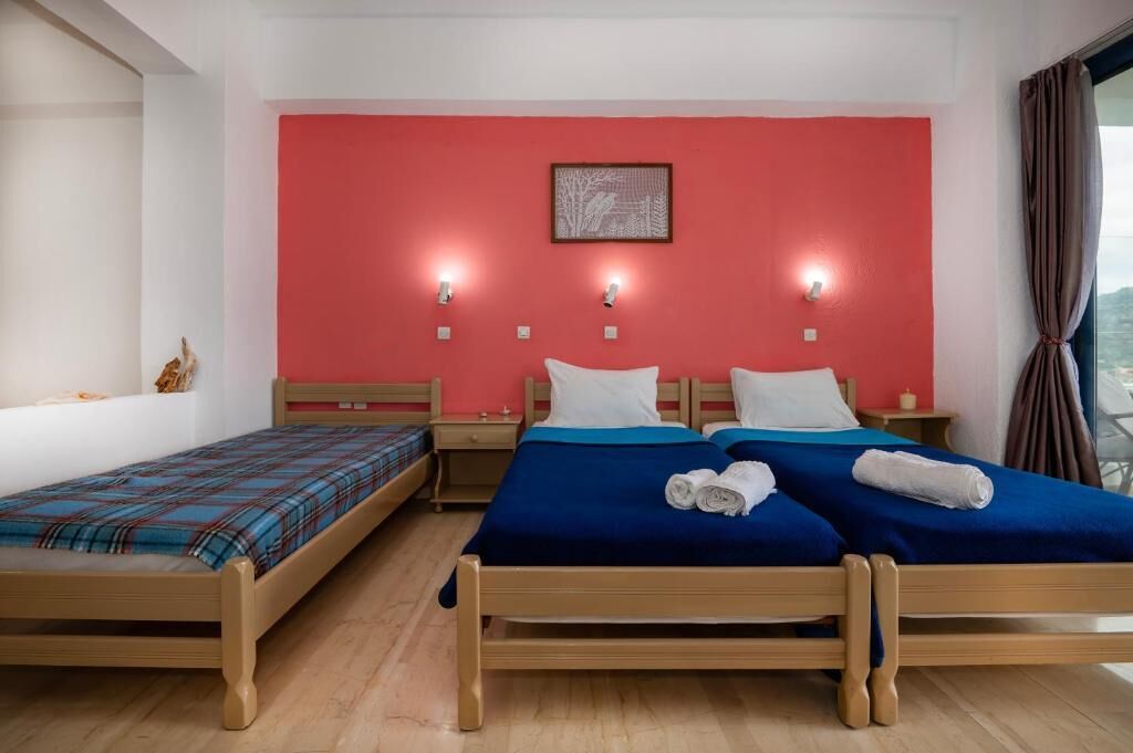 Een hotelkamer met twee eenpersoonsbedden en een tweepersoonsbed, houten meubels, een rode accentmuur en een lijst met een afbeelding.