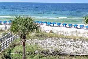A beach with blue umbrellas and a wooden walkway leading to the shore. - Third Floor Oceanfront Condo with Ocean View, Shared Pool, W&D, and Fast WiFi (Fort Walton Beach)