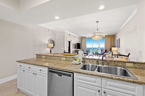 A modern kitchen with granite countertops, stainless steel appliances, and a large window offering a view. - Third Floor Oceanfront Condo with Ocean View, Shared Pool, W&D, and Fast WiFi (Fort Walton Beach)