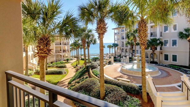 Een hotel binnenplaats met palmbomen, een fontein en uitzicht op de zee.