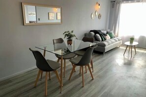 A modern living room with a glass dining table, grey sofa, and a small round table with a plant. - Modern and cozy apartment within walking distance of Escuela Militar Station. (Las Condes)