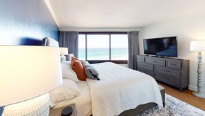 Ein Schlafzimmer mit einem großen Bett, einem Fernseher, einem Schminktisch und Blick aufs Meer.