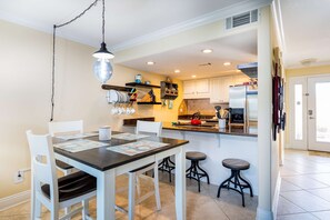A modern kitchen with white cabinetry, a dining table with chairs, and a small bar stool. - Inviting waterfront townhome with full kitchen, balcony, central AC, & W&D (Pensacola Beach)