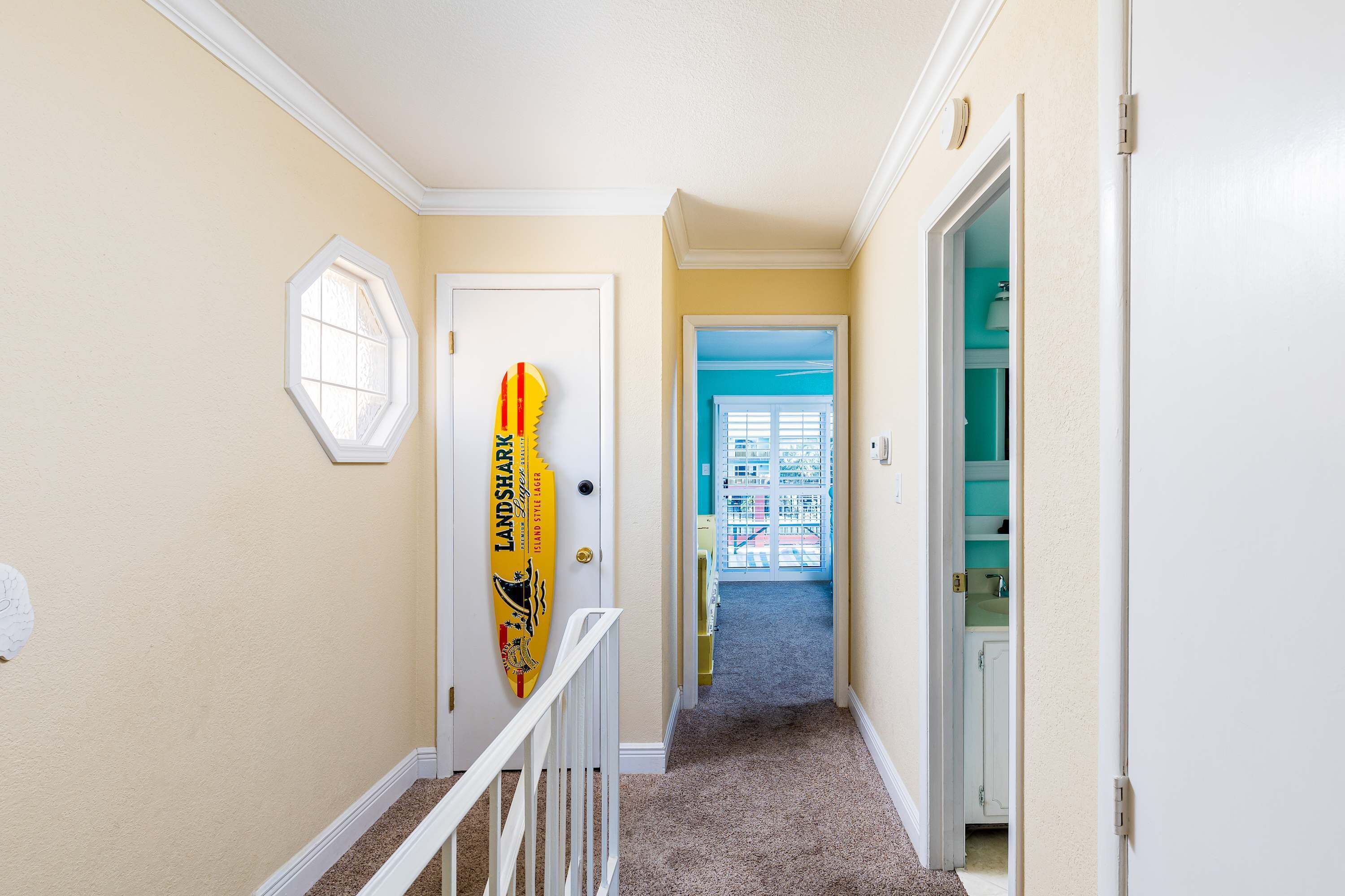 A hallway with a carpeted floor, a white door, and a surfboard leaning against the wall.