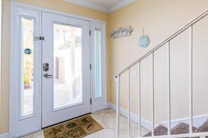A hallway with a white door, a doormat, a wall-mounted clock, and a staircase. - Inviting waterfront townhome with full kitchen, balcony, central AC, & W&D (Pensacola Beach)