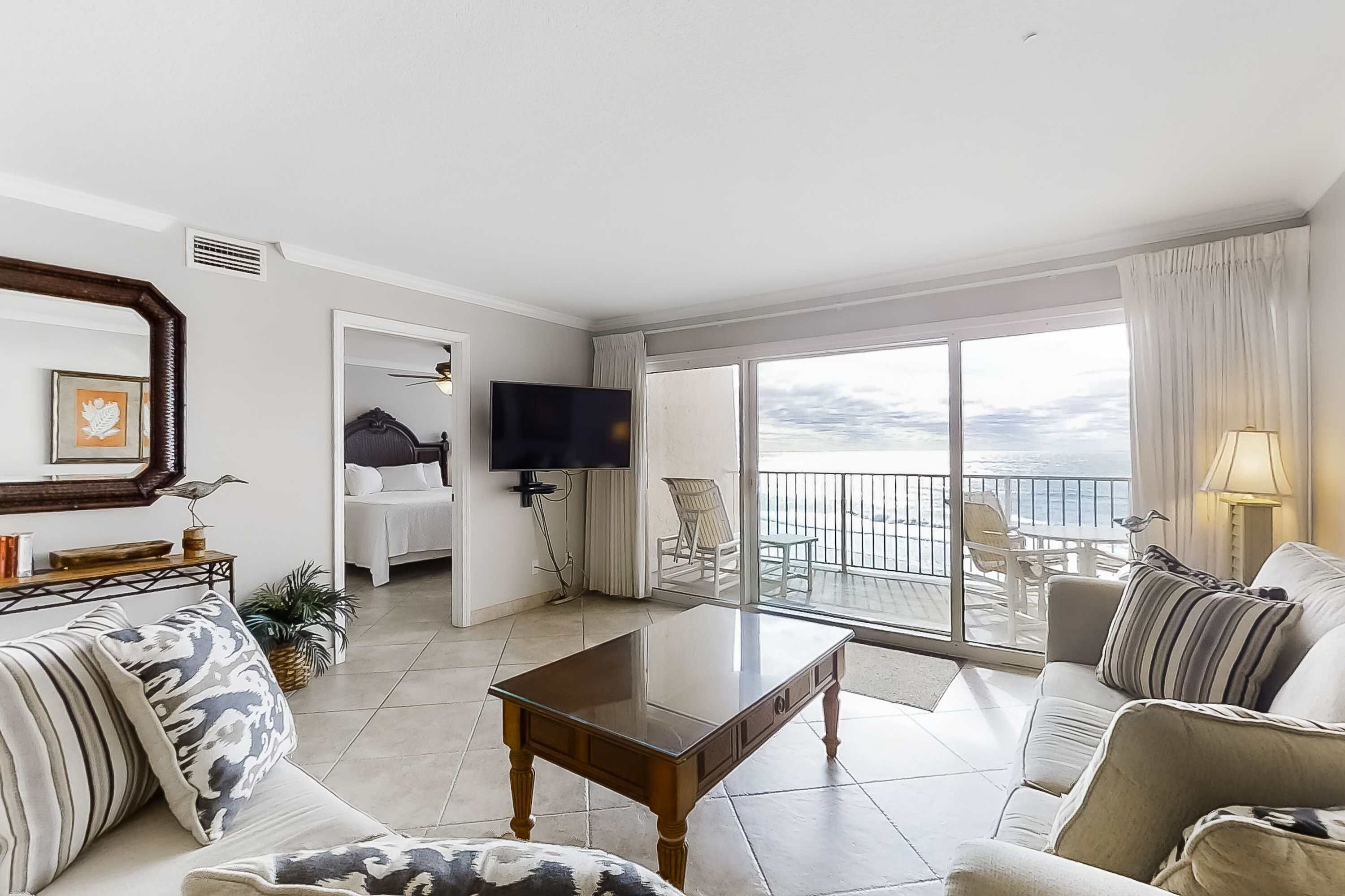 A spacious living room with a large sliding glass door leading to a balcony with a view of the ocean.
