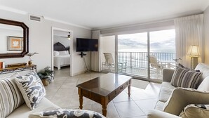 Un ampio soggiorno con un'ampia porta scorrevole in vetro che dà su un balcone con vista sull'oceano.
