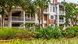 A row of two-story buildings with balconies, surrounded by lush greenery and a white picket fence. - Designer hideaway with outdoor pool, hot tub & gym - walk to dining,shops (Miramar Beach)