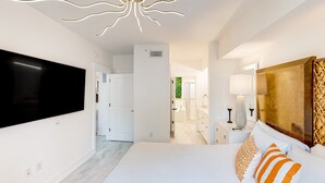 A modern bedroom with a large bed, a flat-screen TV, and a unique ceiling light fixture. - Designer hideaway with outdoor pool, hot tub & gym - walk to dining,shops (Miramar Beach)