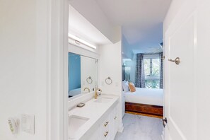 Un baño moderno con tocador blanco, un espejo grande y un lavamanos.