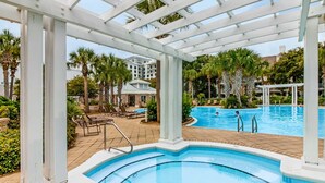 A pool area with a pergola overhead, palm trees, and a view of a building in the background. - Designer hideaway with outdoor pool, hot tub & gym - walk to dining,shops (Miramar Beach)