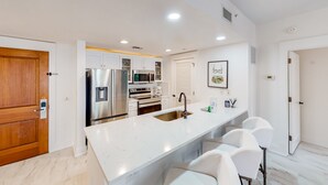 A modern kitchen with white cabinetry, stainless steel appliances, and a marble countertop. - Designer hideaway with outdoor pool, hot tub & gym - walk to dining,shops (Miramar Beach)