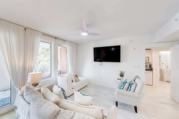 Una sala de estar moderna con sofá, sillón, televisor de pantalla plana y ventilador de techo.