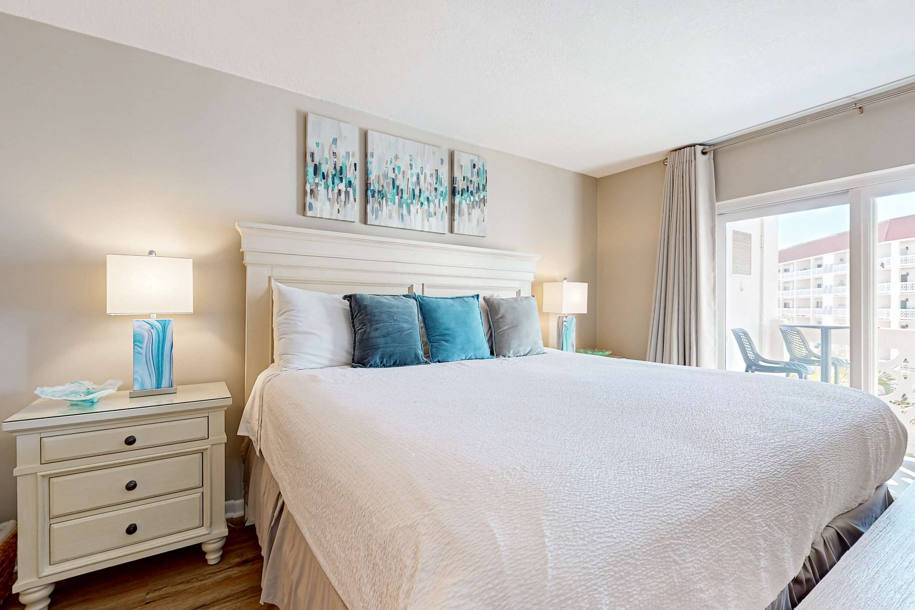 A neatly arranged bedroom with a large bed, two bedside tables with lamps, and a view of the outside balcony.