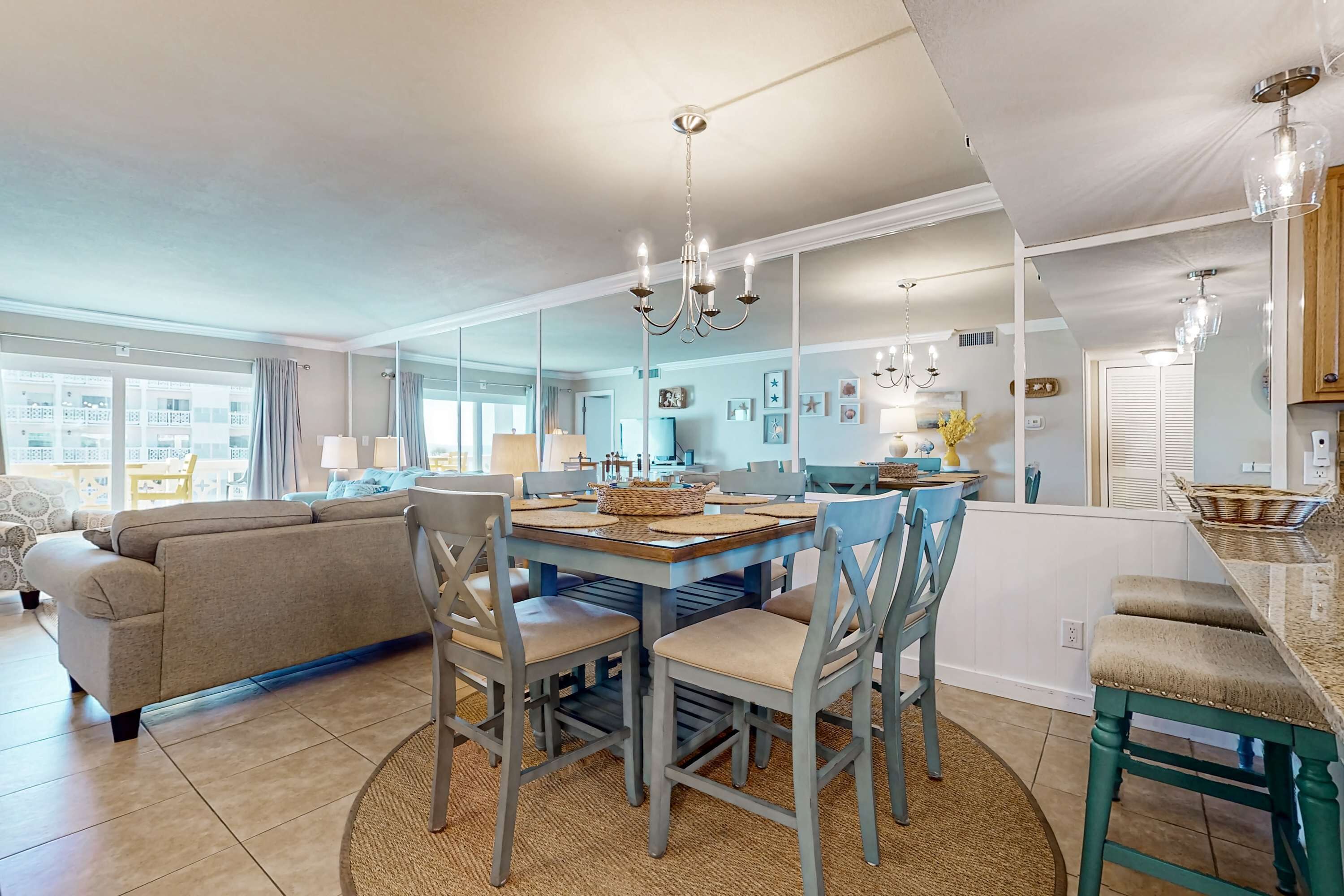 A modern kitchen with a central island, dining area with chairs, and a large mirror reflecting the room.