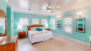 Un dormitorio con ventilador de techo de madera, cama con ropa blanca y cómoda de madera.