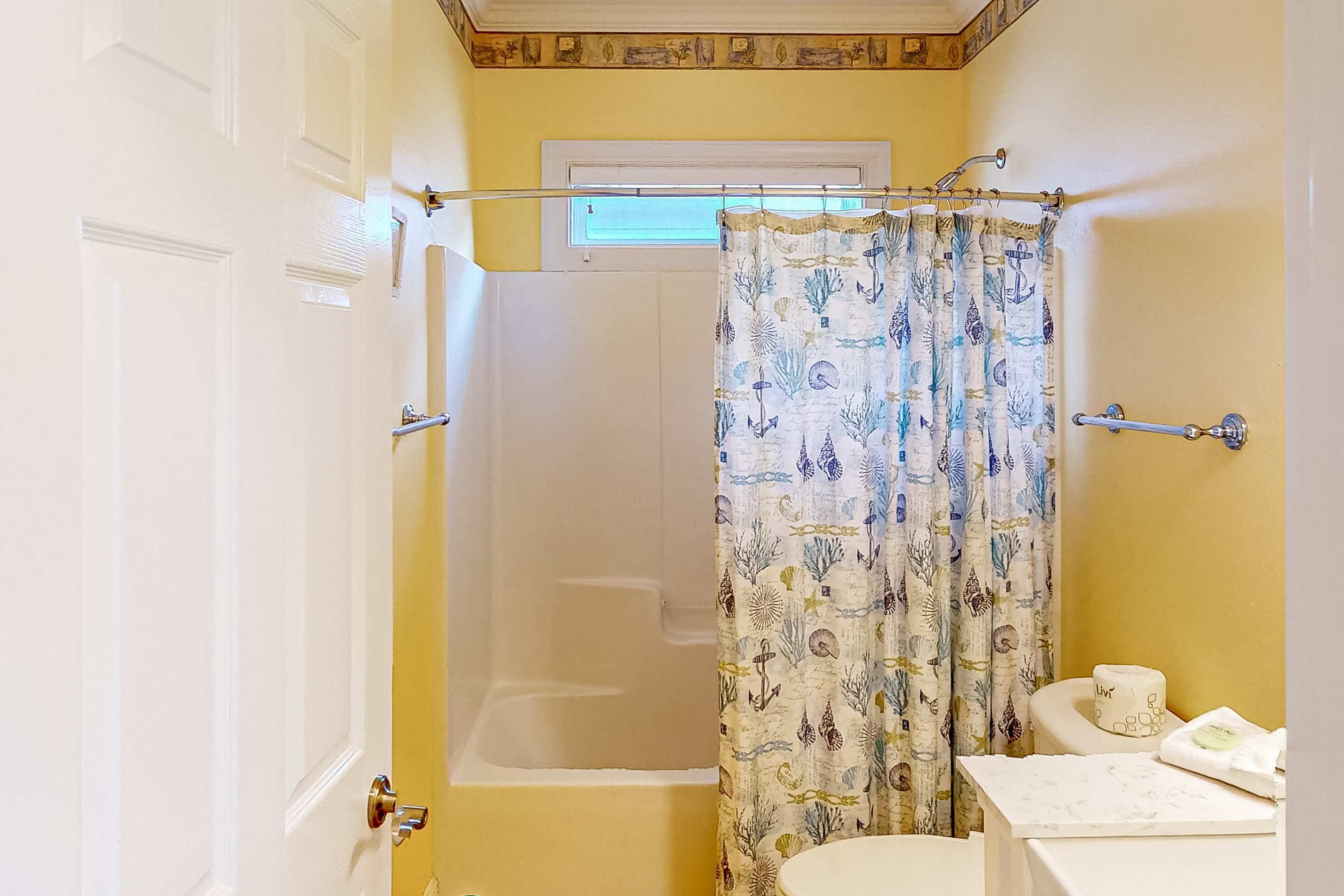 Un baño con bañera, cortina de ducha con motivos acuáticos y un inodoro.