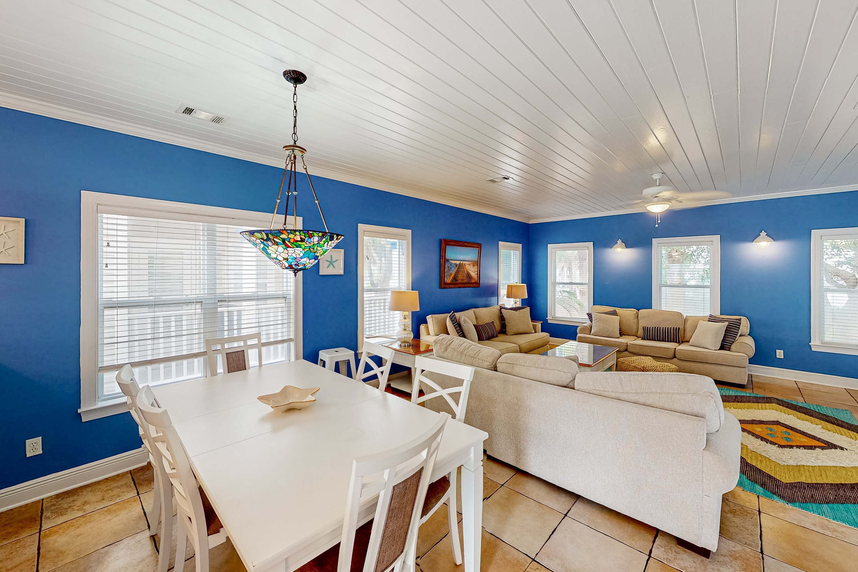 A living room with a blue wall, white ceiling, and a dining area with a white table and chairs.