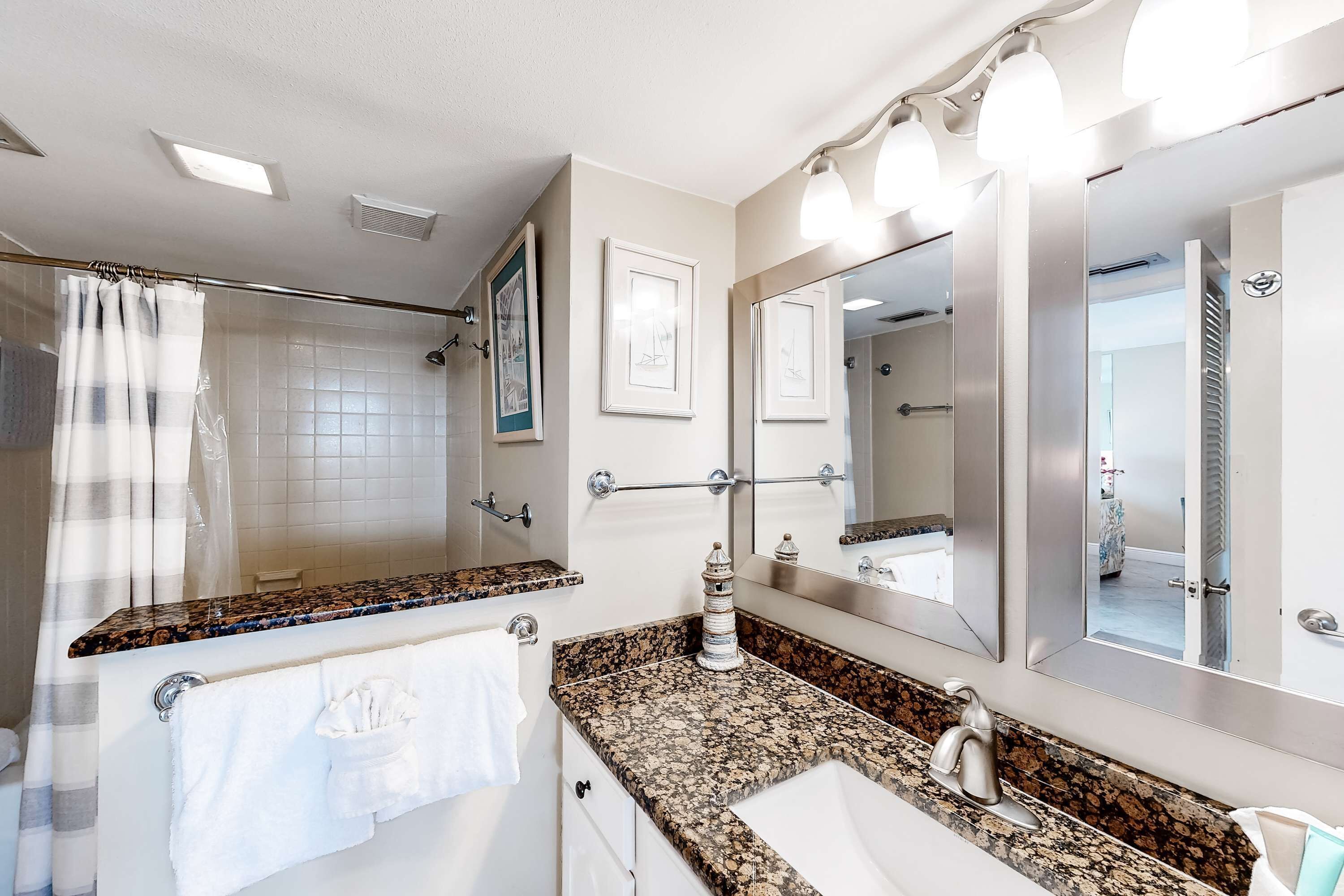 A modern bathroom with a granite countertop, a large mirror, and a shower area.