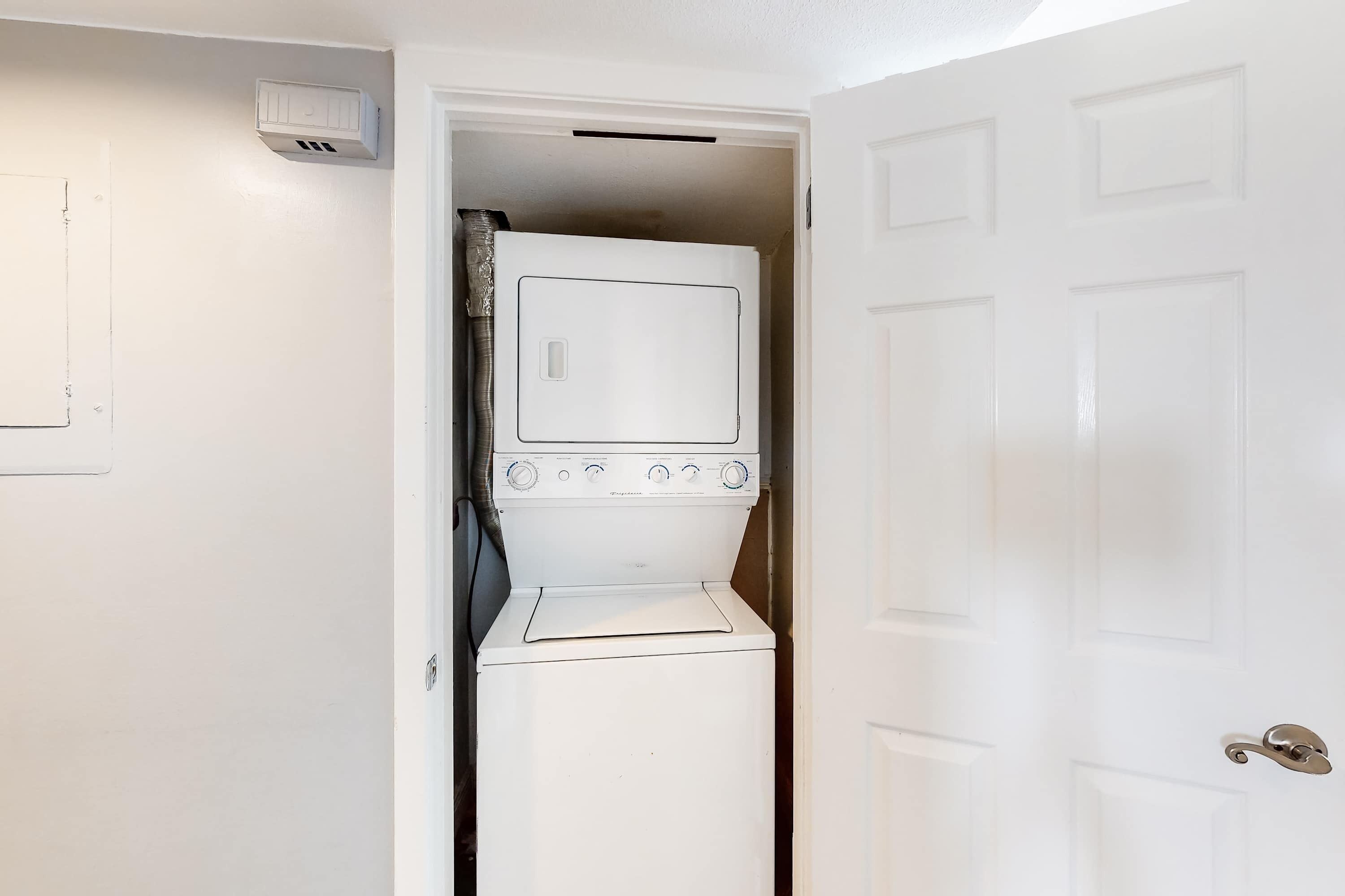 Une petite buanderie équipée d’un lave-linge et d’un sèche-linge encastrés, d’une porte blanche et d’une bouche d’aération fixée au mur.