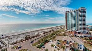 A high-rise hotel with multiple balconies, a beach view, and a parking area with palm trees. - Waterfront condo with WiFi, washer/dryer, pools, fitness room, & beach access (Pensacola Beach)