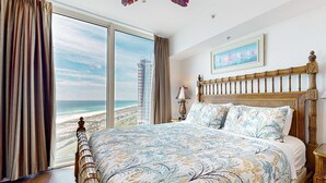 A bedroom with a large bed, a view of the beach, and a painting on the wall. - Waterfront condo with WiFi, washer/dryer, pools, fitness room, & beach access (Pensacola Beach)