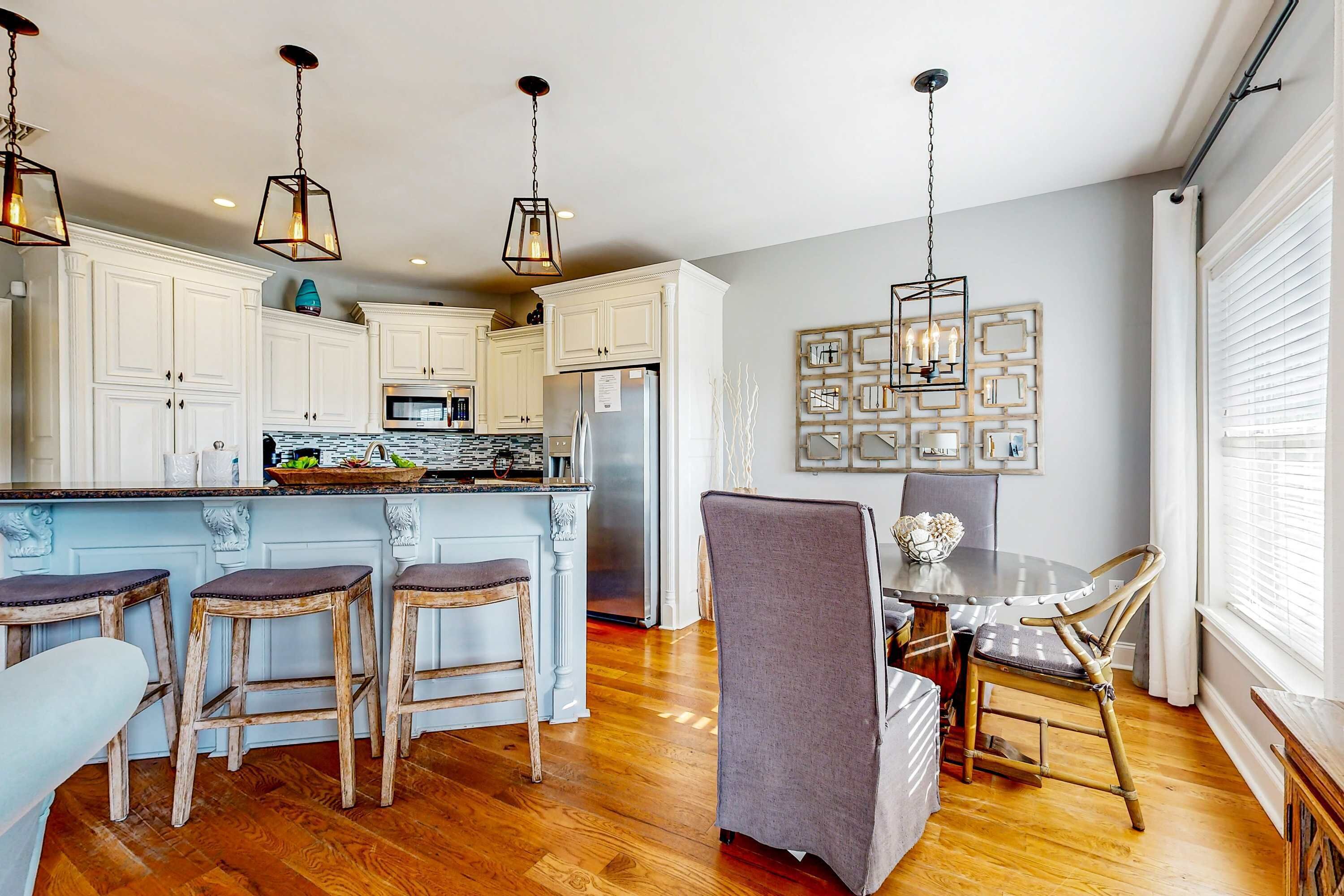 A kitchen with white cabinets, a central island with stools, a refrigerator, and pendant lights.