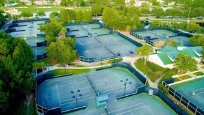 Vue aérienne d’un complexe sportif comprenant plusieurs courts de tennis, entouré d’arbres et de bâtiments.