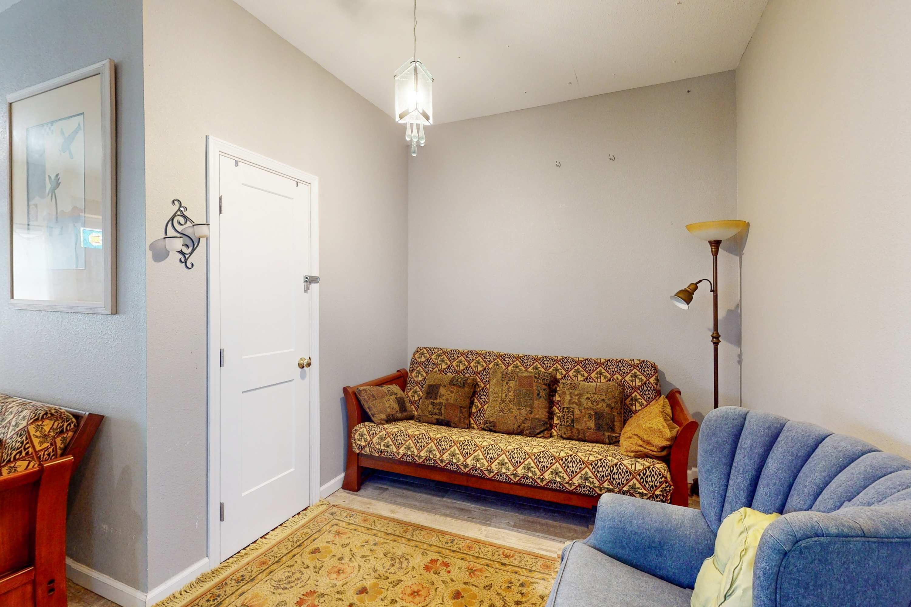 A living room with a sofa, a chair, a table, a patterned rug, a door, and a floor lamp.