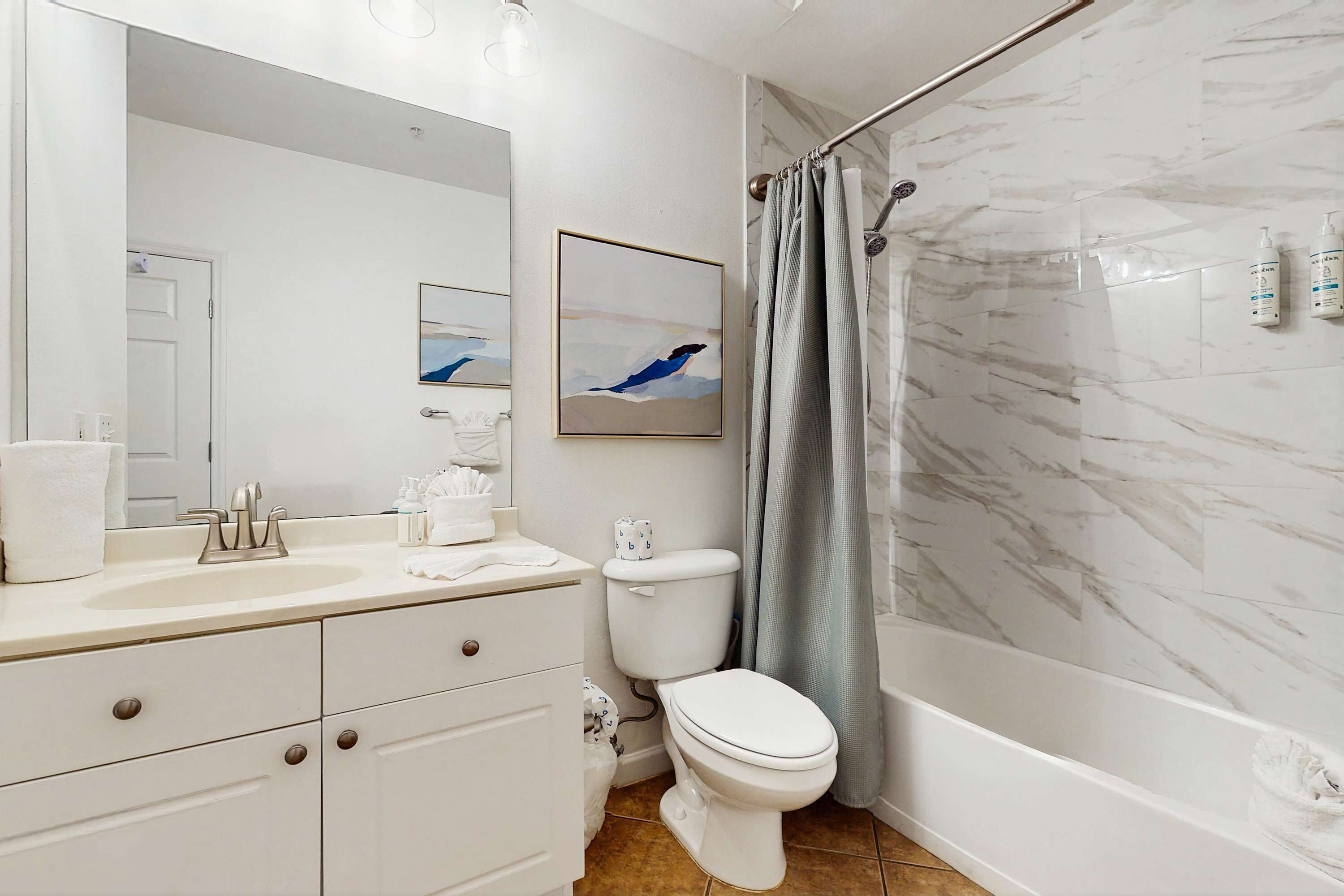 Ein modernes Badezimmer mit Waschbecken, Toilette und Badewanne in Weiß. Ein Duschvorhang und ein gerahmtes Bild sind an der Wand angebracht.