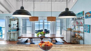 A dining area with a wooden table, two hanging pendant lights, and a bowl of fruit on the table. - Dog-friendly with Gulf view, pool, balcony, deck, fireplace, central AC, & W&D (St. George Island)