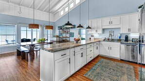 A spacious kitchen with white cabinets, a large island, hanging pendant lights, and a view to the outside. - Dog-friendly with Gulf view, pool, balcony, deck, fireplace, central AC, & W&D (St. George Island)