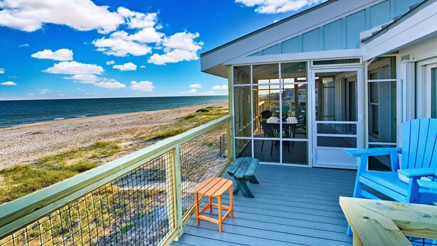 A balcony with a view of the beach and ocean, featuring a table, chairs, and a small stool. - Dog-friendly with Gulf view, pool, balcony, deck, fireplace, central AC, & W&D (St. George Island)