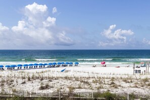 A beach with white sand, a wooden fence, and a row of blue umbrellas. - Beautiful coastal retreat with water view, beach access, & shared pool,hot tub (Fort Walton Beach)