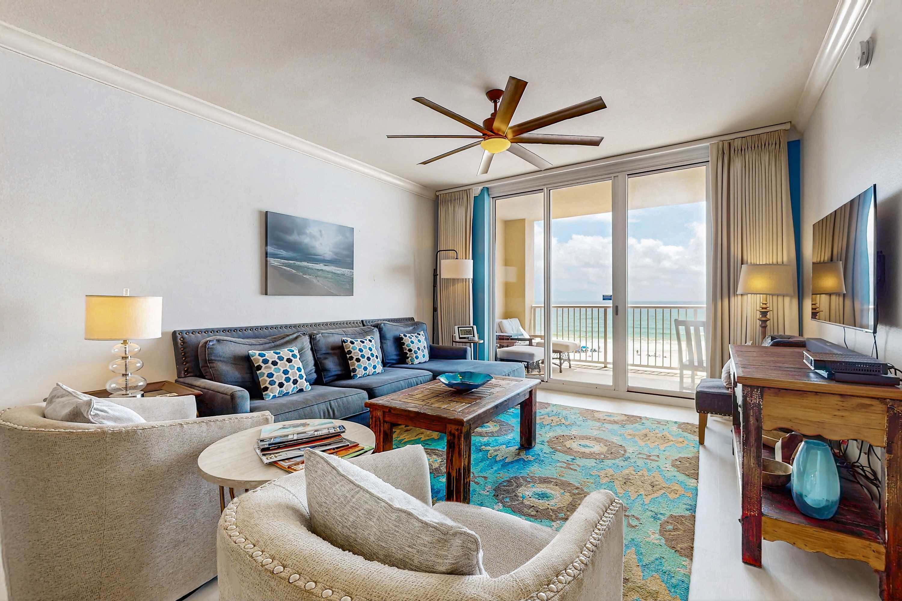A hotel room with a sofa, armchair, coffee table, and a balcony with a view.