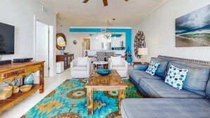 Een woonkamer met een blauwe bank, een houten salontafel en een plafondventilator.