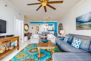 A living room with a blue sofa, a wooden coffee table, and a ceiling fan. - Gulf Front Condo, Beach Service Included, Walk To Dining & Entertainment (Fort Walton Beach)