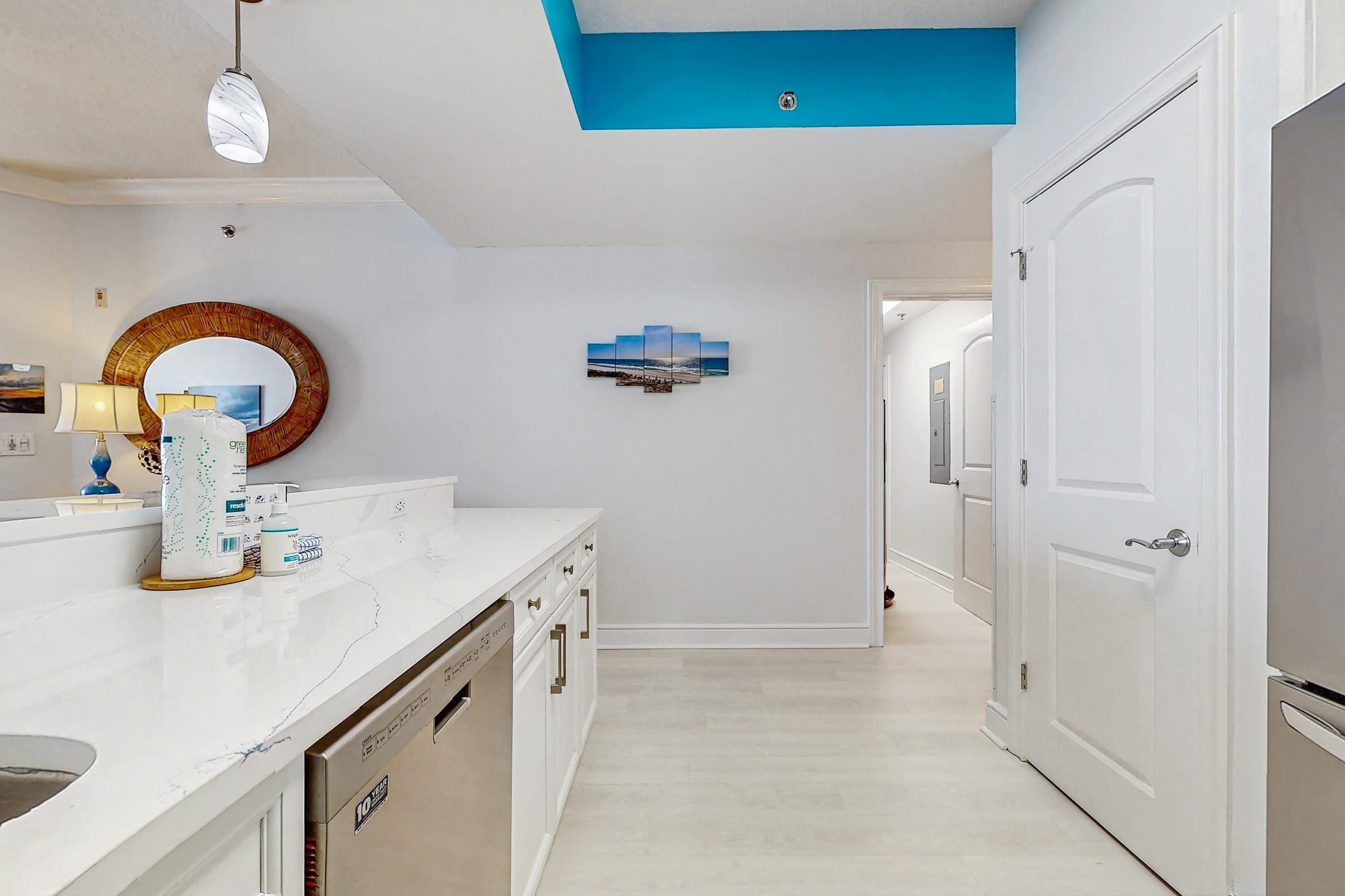 A modern kitchen with white countertops, a dishwasher, and a blue accent wall.