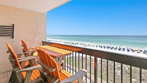 Een balkon met een houten tafel en stoelen, met uitzicht op een strand met parasols en mensen.