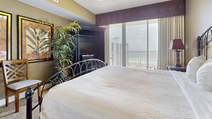 A hotel room with a large bed, a television, a chair, a plant, and a balcony with curtains. - Family-friendly 13th-floor condo w/furnished balcony, shared tennis, and pool (Miramar Beach)