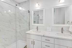 Une salle de bain moderne dotée d’une douche à parois de verre, d’un meuble-lavabo blanc avec deux vasques et d’un grand miroir au-dessus du meuble-lavabo.