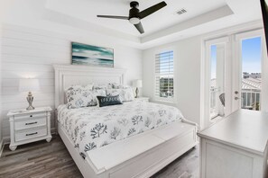 Une chambre à coucher avec un lit, des tables de chevet, un ventilateur de plafond, une fenêtre et une vue sur l’extérieur.