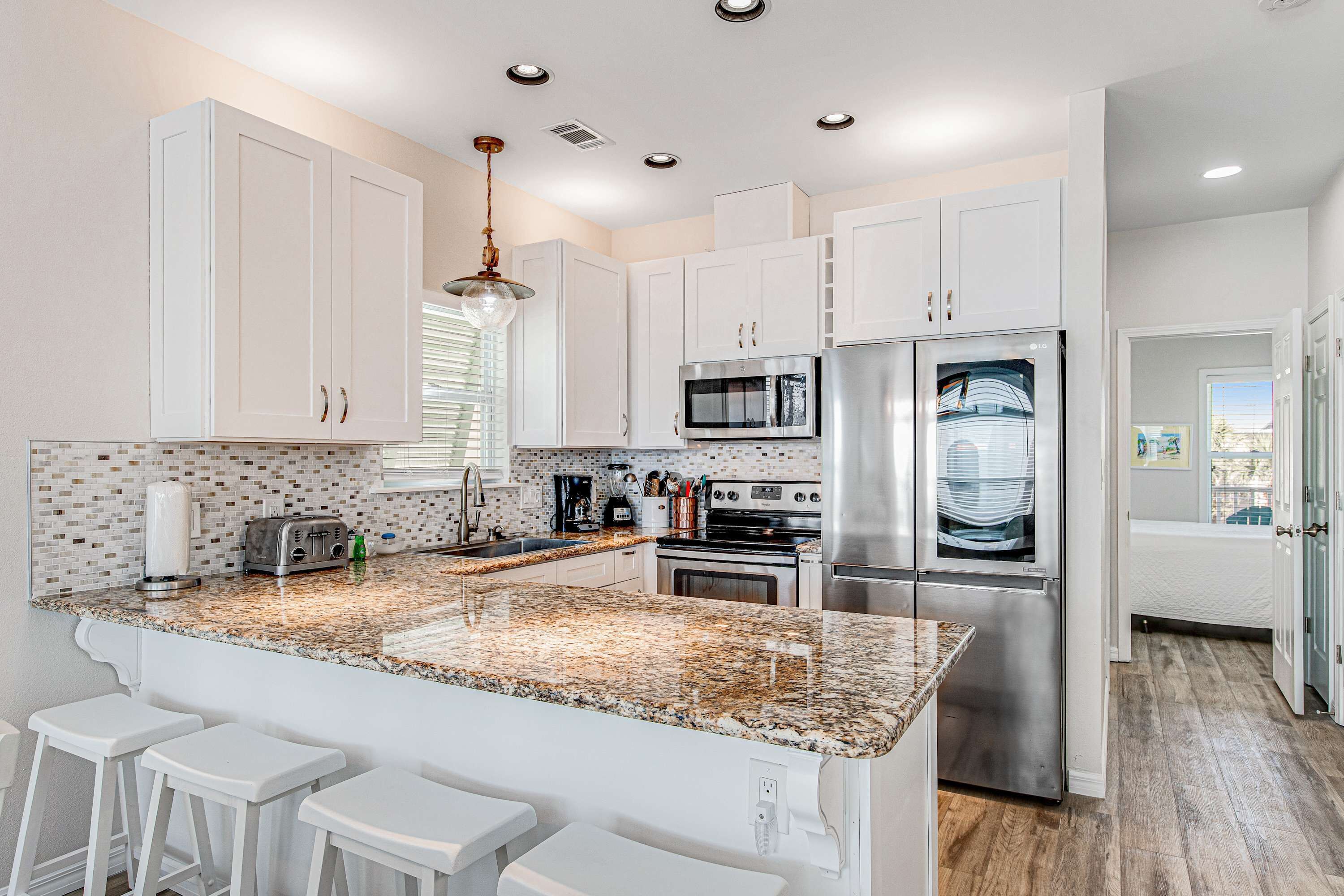 A modern kitchen with white cabinets, granite countertops, stainless steel appliances, and a bar area with stools.