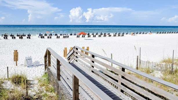 A beach with a wooden boardwalk leading to the water, white sand, and umbrellas. - Delightful condo with pools, hot tub, tennis court, grilling area (Miramar Beach)